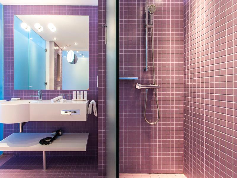 Bagno d'hotel moderno con piastrelle viola, doppi lavandini e doccia a filo pavimento.