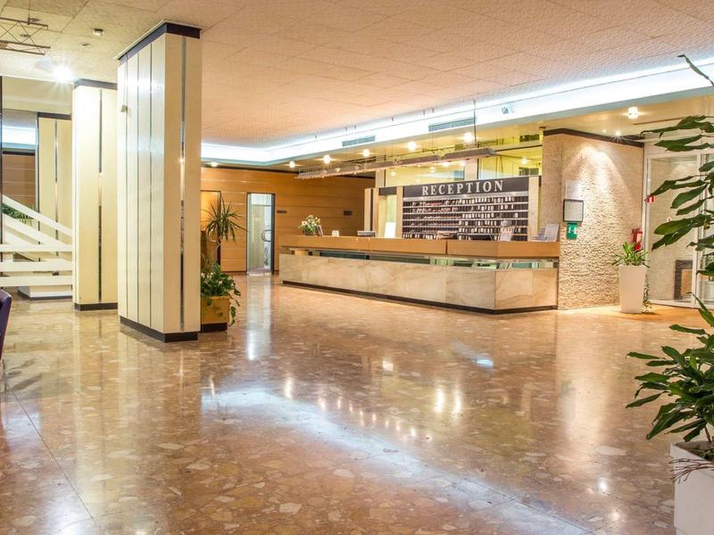 Ampia hall d'hotel luminosa con reception, area salotto, pianta, design moderno e pavimento in marmo.