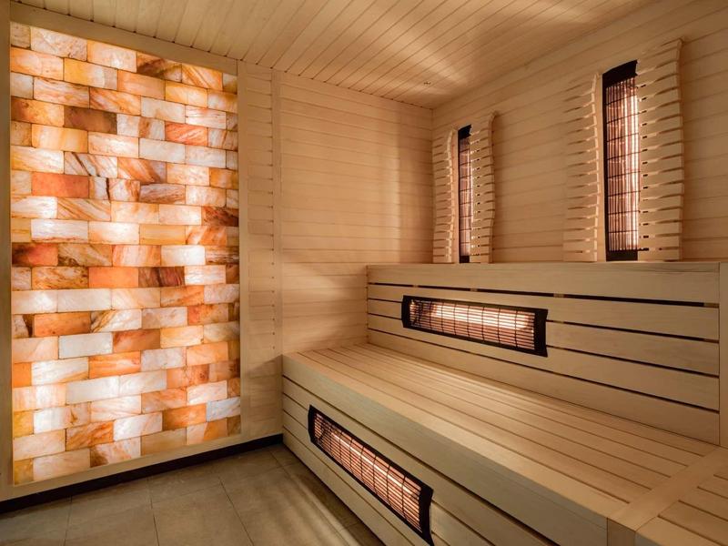Moderní sauna s dřevěnými lavicemi a osvětlenými solnými stěnovými panely.