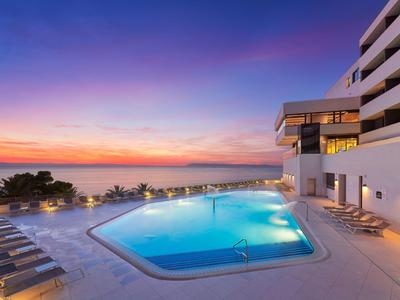Hotelpool mit Sonnenliegen bei Sonnenuntergang, Blick aufs Meer.