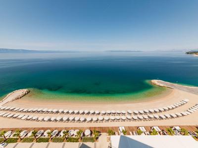 Strand mit Reihen von Liegestühlen und Schirmen vor ruhigem blauem Meer bei klarem Himmel.