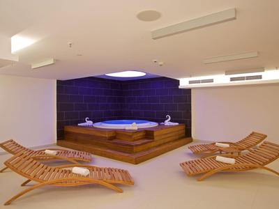 Moderner Wellnessbereich mit Whirlpool auf Podest und Liegestühlen mit Handtüchern.