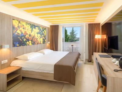 Modernes Hotelzimmer mit Doppelbett, Schreibtisch, TV und Balkon mit Ausblick auf Bäume.