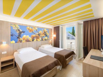 Helles Hotelzimmer mit zwei Einzelbetten, großes Blumenbild und Zugang zu Balkon.