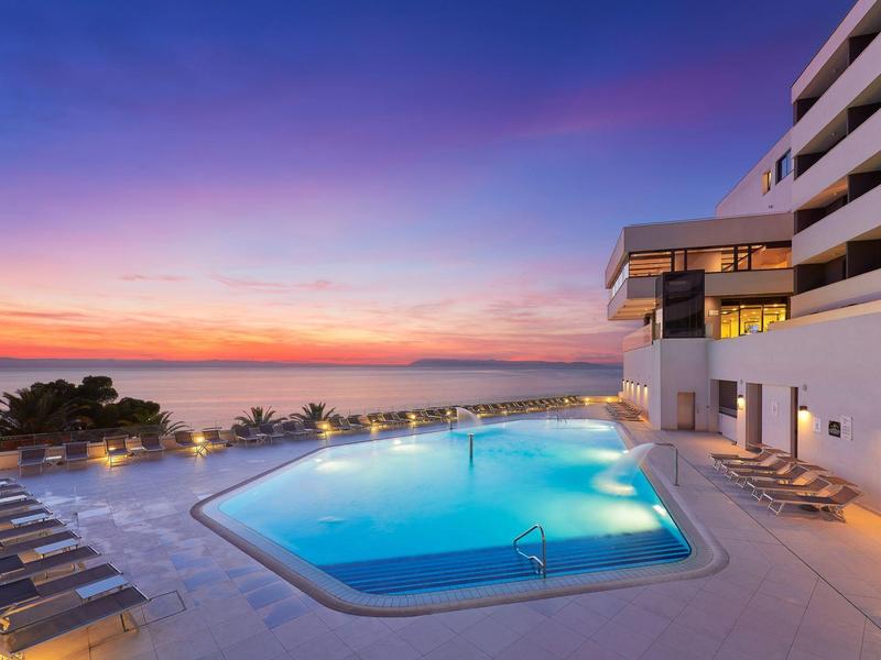 Hotelpool mit Sonnenliegen bei Sonnenuntergang, Blick aufs Meer.