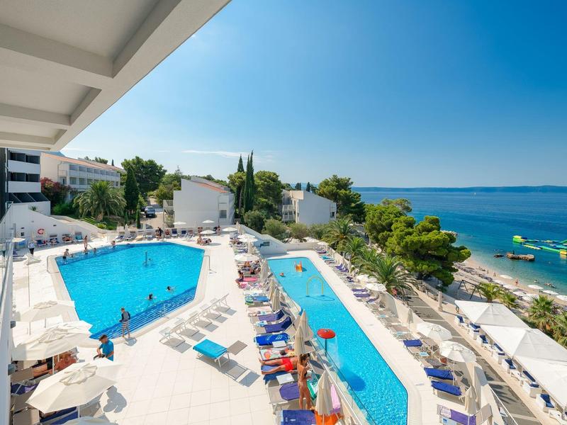 Hotelterrasse mit zwei Pools, Sonnenliegen und Blick aufs Meer.