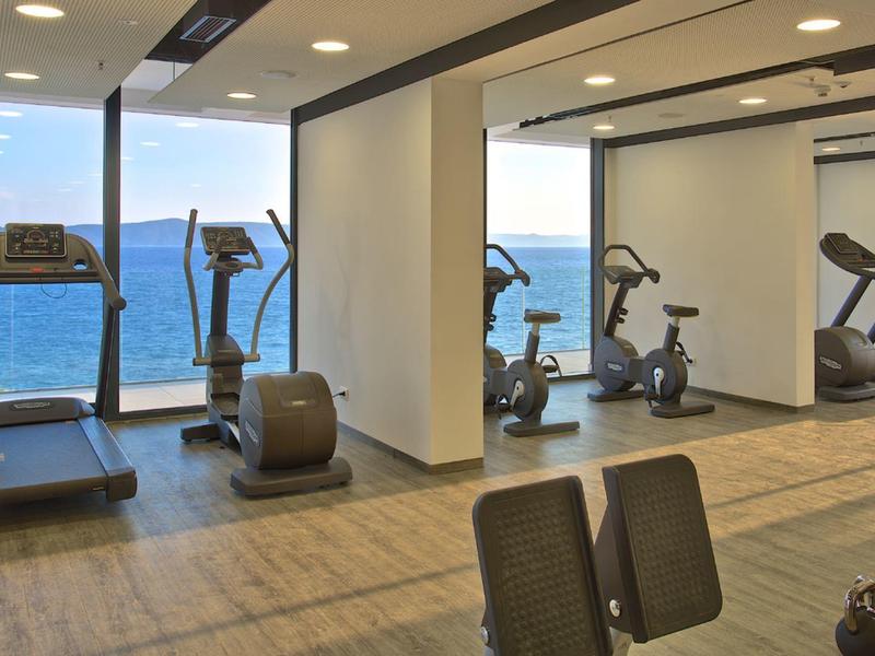 Helles Fitnessstudio mit modernen Geräten und Meerblick durch große Fenster.