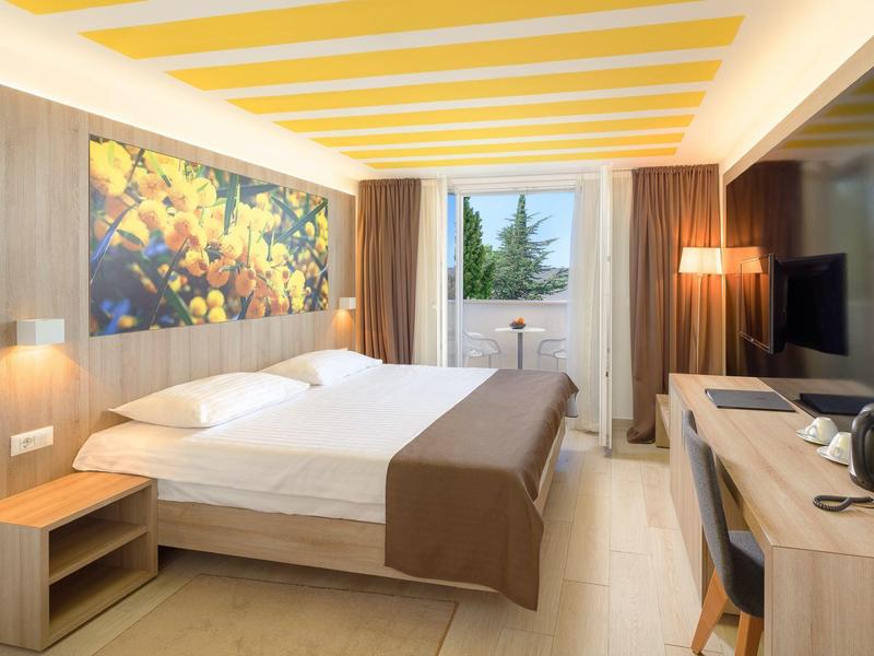 Modernes Hotelzimmer mit Doppelbett, Schreibtisch, TV und Balkon mit Ausblick auf Bäume.