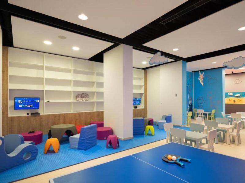 Bunter Kinderspielbereich mit Sitzkissen, Tischen und Spielzeug in einem Hotel.