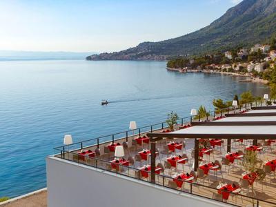Terrazza dell'hotel con sedie rosse con vista sul mare calmo e sulla costa.