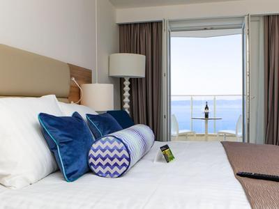 Modern hotelkamer met groot bed en uitzicht op zee door een glazen schuifdeur.