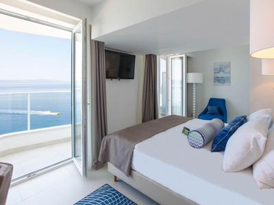 Lichte hotelkamer met balkon en uitzicht op zee, wit bed met blauwe accenten.