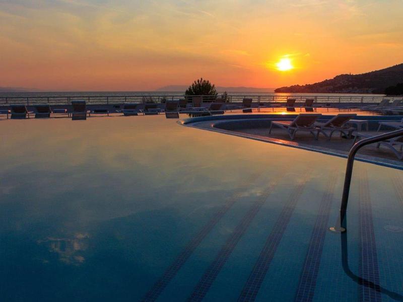 Coucher de soleil sur une piscine calme avec des chaises longues et vue sur la mer.