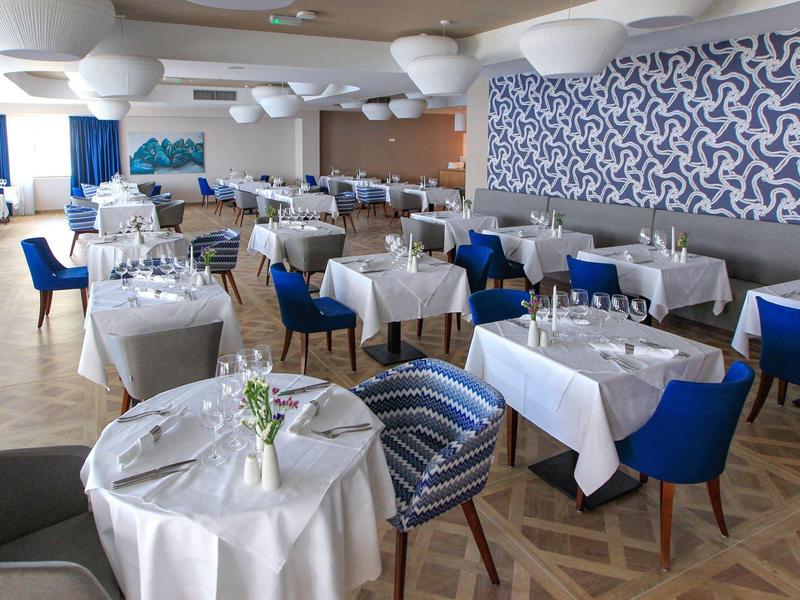 Restaurant lumineux avec nappes blanches, chaises bleues et décoration murale moderne.