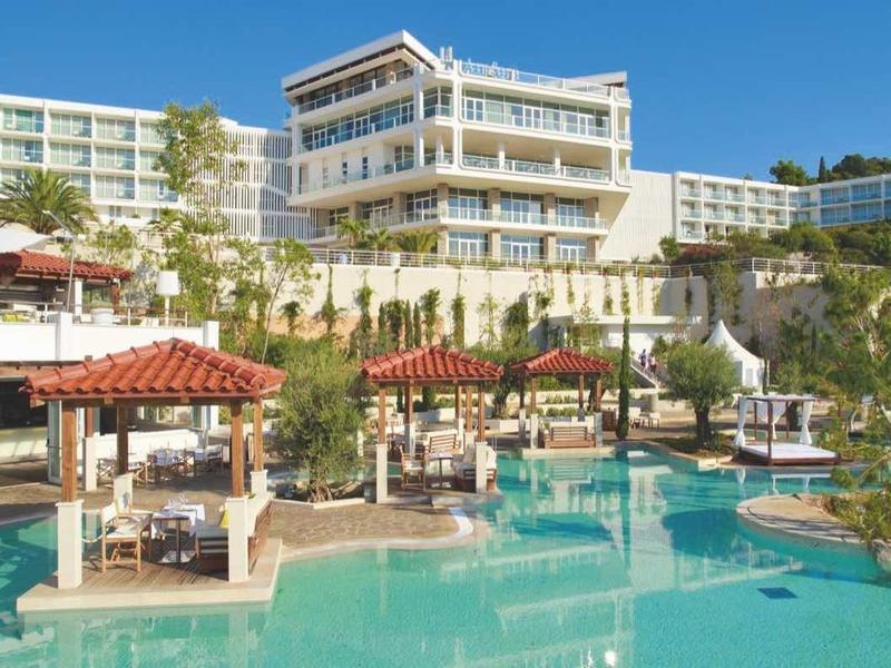 Hôtel de luxe avec grandes piscines, parasols et palmiers sous un ciel bleu clair.