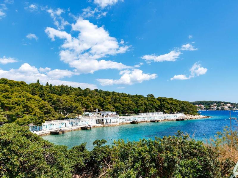 Littoral avec bâtiments blancs, mer bleue et colline boisée sous ciel bleu.