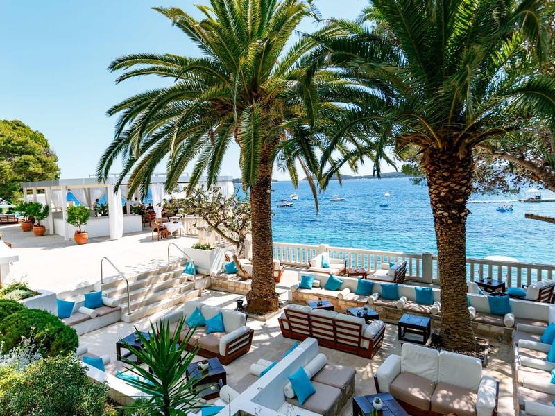 Terrasse d'hôtel avec palmiers et sièges extérieurs donnant sur la mer.