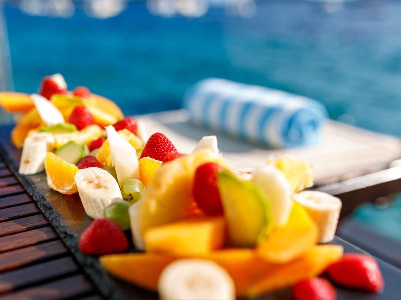 Morceaux de fruits colorés sur une table en bois avec vue sur l'eau et une serviette en arrière-plan.