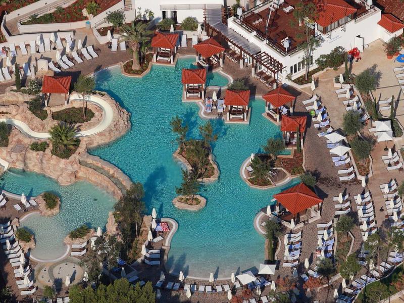 Vue aérienne d'une piscine de complexe avec îles, pavillons rouges et chaises longues.