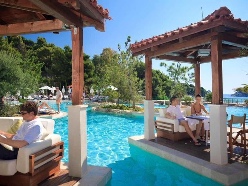Espace détente avec piscine, meubles en bois et vue sur la mer sous un ciel clair.