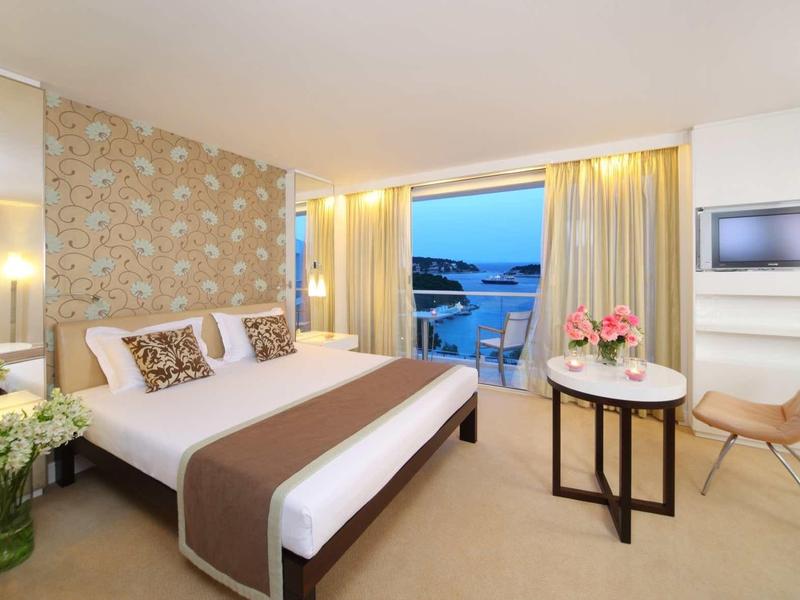 Chambre d'hôtel moderne avec lit double, balcon et vue sur la mer au coucher du soleil.