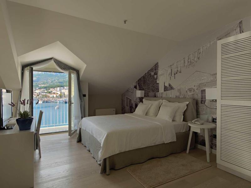 Modern eingerichtetes Schlafzimmer mit großem Bett, Balkon und Blick auf Wasser und Berge.