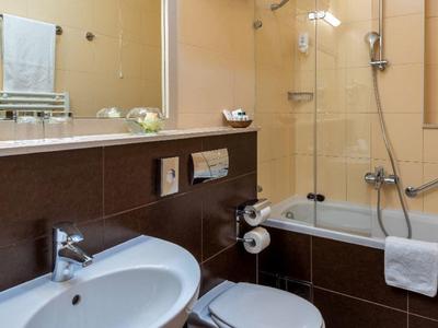 Salle de bain moderne d'hôtel avec baignoire, douche, lavabo et toilettes aux tons chauds.