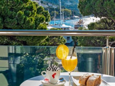 Table avec café, jus d'orange et pâtisserie sur un balcon avec vue sur le port et les voiliers.