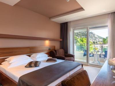 Chambre d'hôtel moderne avec lit double, fauteuil et balcon avec vue sur la montagne.