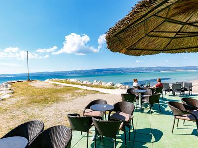Terrasse mit Tischen und Stühlen am Meer unter blauem Himmel und Strohdach
