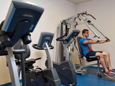 Mann trainiert an einem Fitnessgerät in einem hellen Fitnessraum mit blauen Böden.