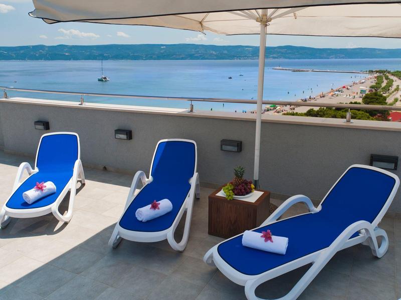 Trois chaises longues bleues sur une terrasse avec vue sur la mer et parasol.