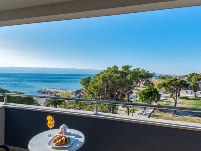 Balcon avec table et petit-déjeuner avec vue sur la mer et des arbres côtiers.
