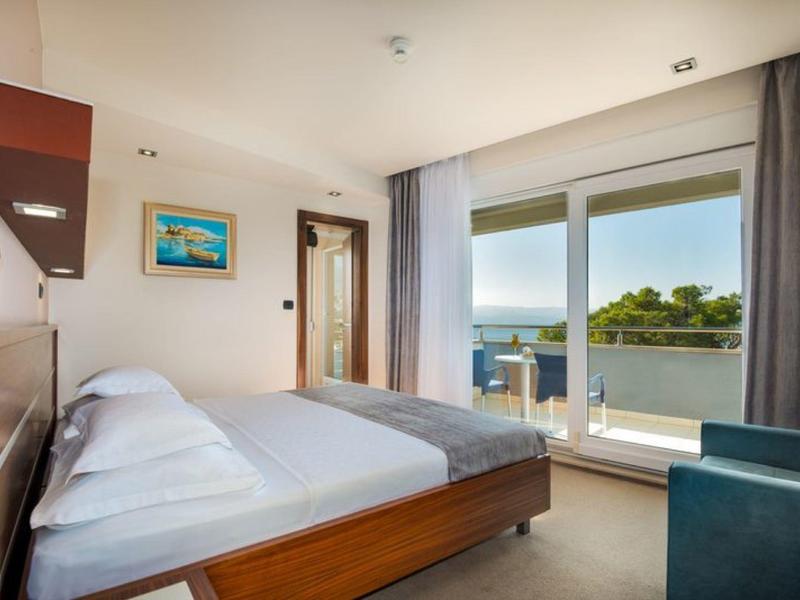 Chambre d'hôtel moderne avec lit double, fauteuil et balcon avec vue sur la mer.