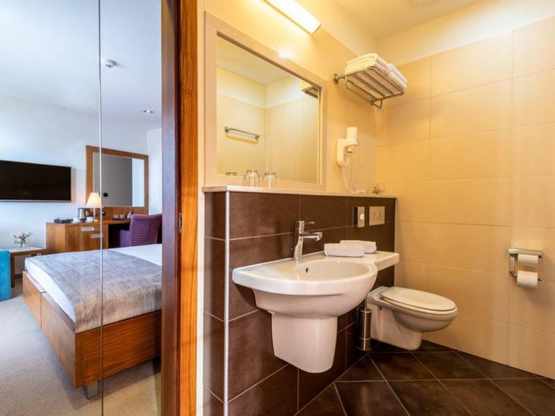 Salle de bain moderne attenante avec lavabo et WC, vue sur chambre d'hôtel lumineuse.