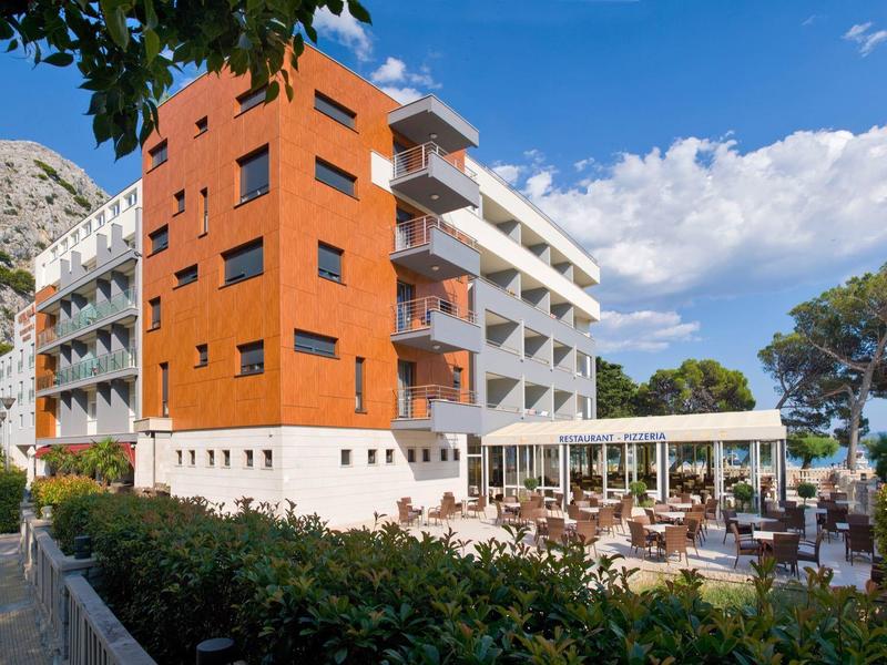 Bâtiment hôtelier moderne avec terrasse et restaurant, montagnes en arrière-plan.