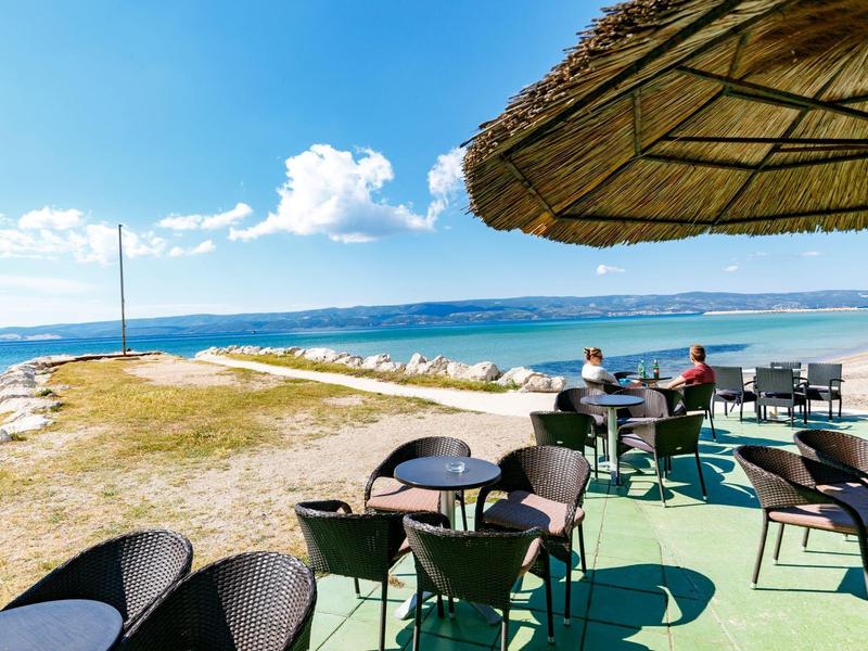 Terrasse avec chaises et tables sur la plage avec vue sur la mer et ciel bleu.