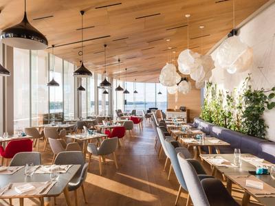 Modern hotel restaurant with wooden floor, many tables, and large windows letting in daylight.