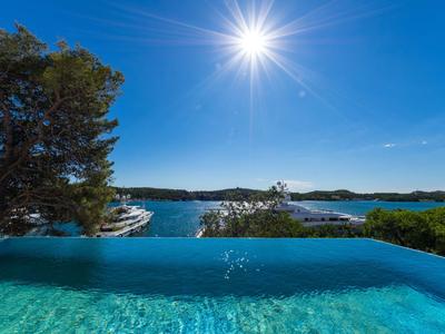 Infinity pool overlooking the sea, surrounded by green trees and a clear sky.