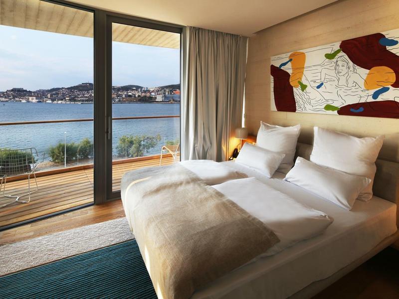 Chambre d'hôtel moderne avec grand lit, balcon et vue sur la mer.