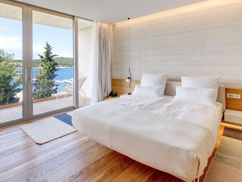 Chambre d'hôtel moderne avec grand lit et vue sur la mer à travers des fenêtres du sol au plafond.