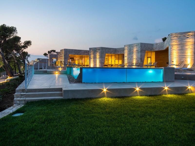 Villa moderne avec piscine éclairée et pelouse soignée au crépuscule.