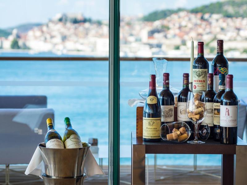 Bouteilles de vin et seau à vin sur des tables avec vue sur la mer et paysage côtier en arrière-plan.