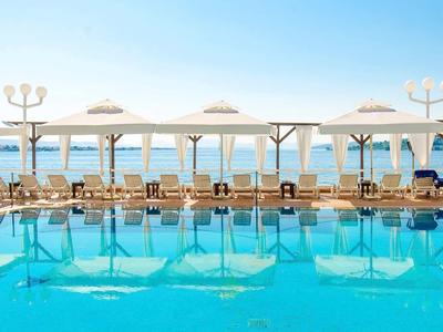 Duży basen hotelowy z leżakami i parasolami przy morzu pod czystym niebem.