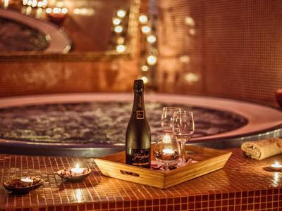 Drewniana taca z butelką wina, kieliszkami i świecą przed podgrzewanym jacuzzi z mozaikowych płytek.