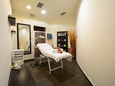 Prosty pokój zabiegowy spa z łóżkiem, lustrem i półkami z produktami.