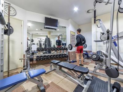 Ein moderner Fitnessraum mit Geräten und einer Person in Sportkleidung vor einem Spiegel.