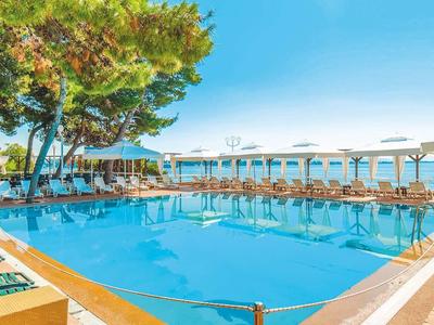 Grande piscina all'aperto con lettini e ombrelloni sotto gli alberi e cielo azzurro