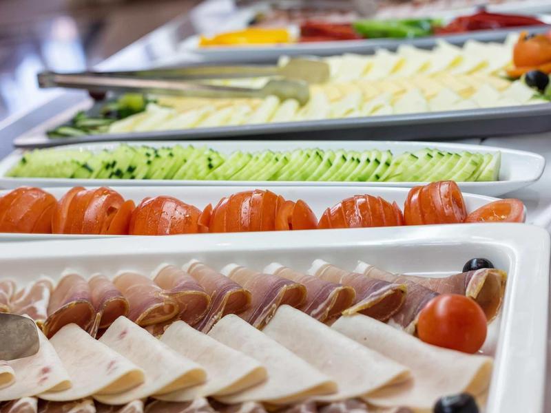 Różne plastry sera, wędlin i warzyw ułożone na białych półmiskach.