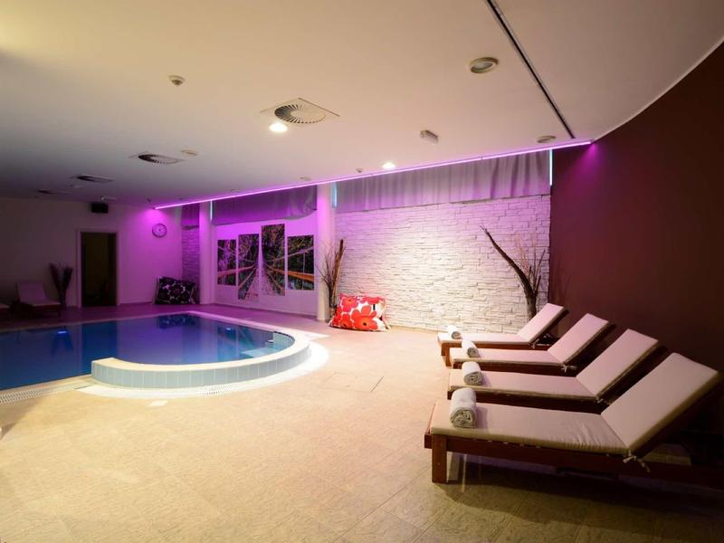 Wnętrze z basenem i leżakami, fioletowe oświetlenie ścienne tworzące nowoczesną, relaksującą atmosferę.